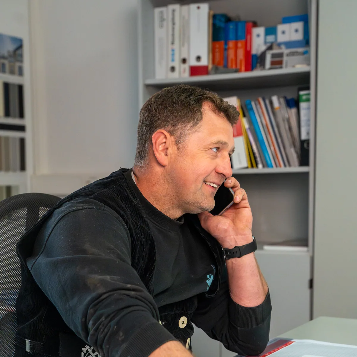 Zimmermeister Sven Hinrichs telefoniert im Büro der Zimmerei Der Holzprofi und blickt auf Baupläne