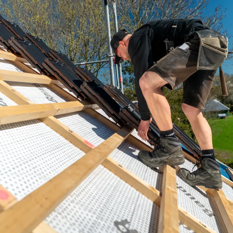 Zimmerer der Zimmerei Der Holzprofi verlegt Konterlattung und Dachziegel auf einer Wohnhaus-Baustelle — Referenz Dacharbeiten