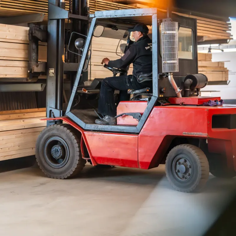 Mitarbeiter der Zimmerei Der Holzprofi fährt mit dem Gabelstapler durch das Holzlager der Werkstatt