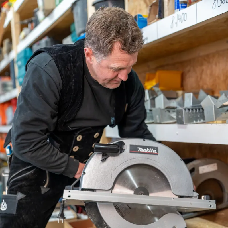 Zimmermeister Sven Hinrichs sägt mit der Makita-Handkreissäge einen Holzbalken in der Werkstatt der Zimmerei Der Holzprofi
