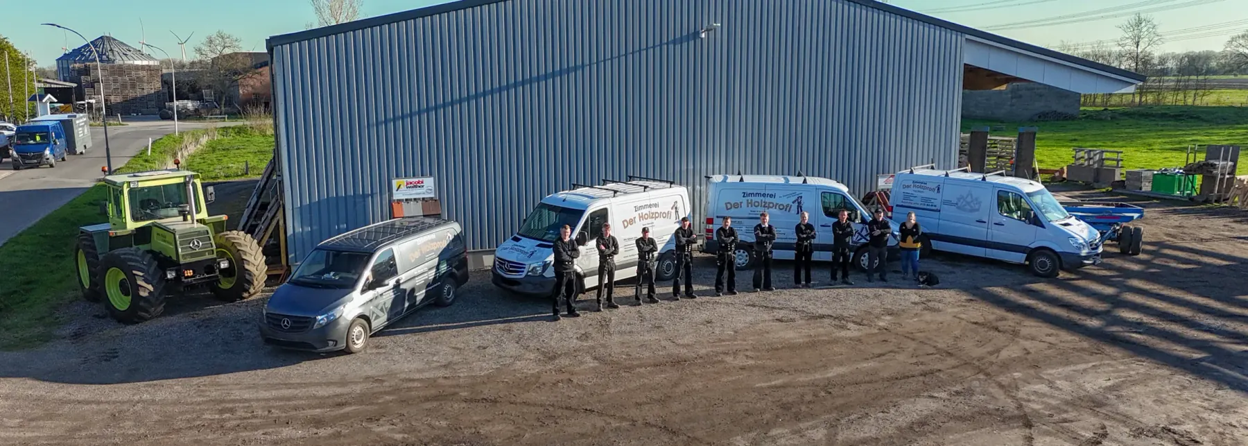Das vollständige Team der Zimmerei Der Holzprofi mit Fuhrpark vor der Werkstatthalle in Bargenstedt