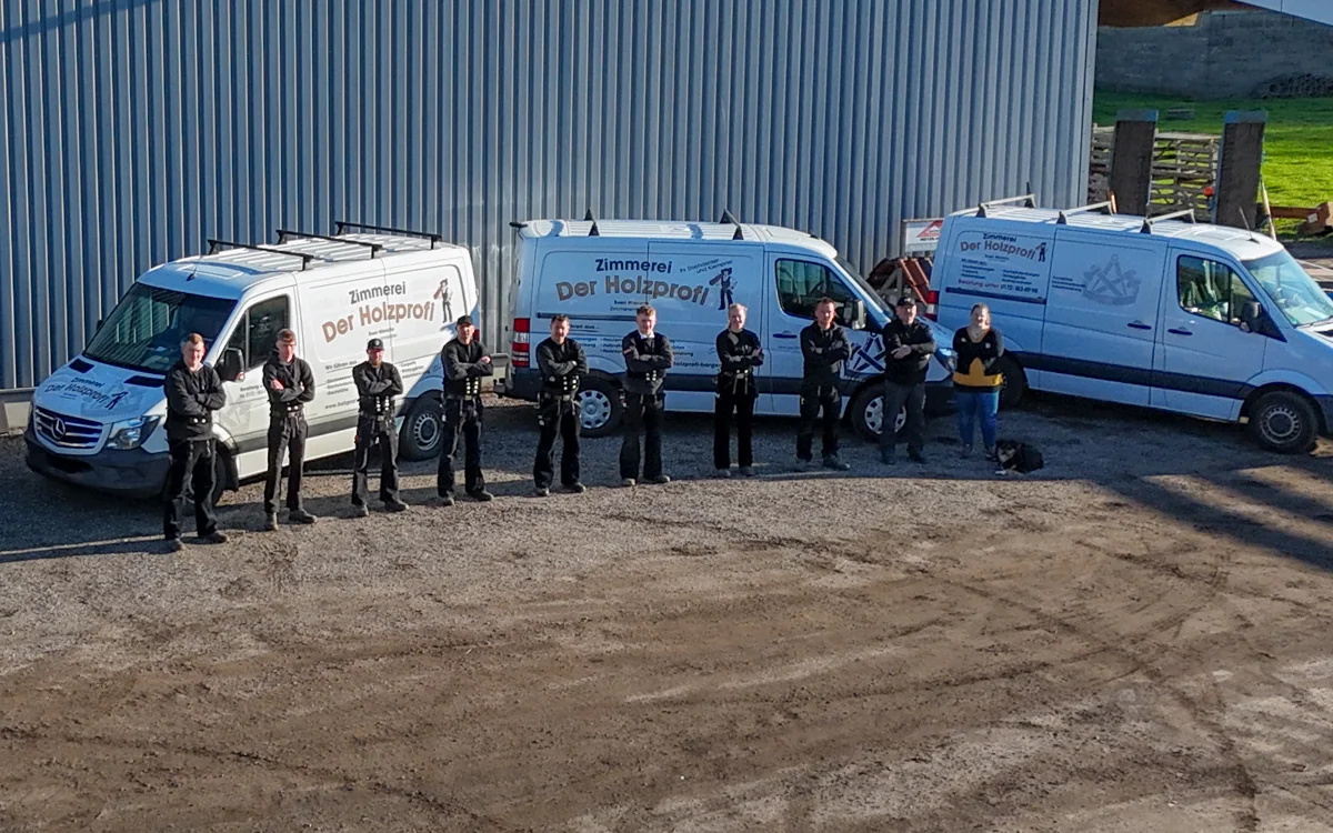 Zimmerer-Team der Zimmerei Der Holzprofi vor den gebrandeten Firmenfahrzeugen am Werkstattgebäude in Bargenstedt